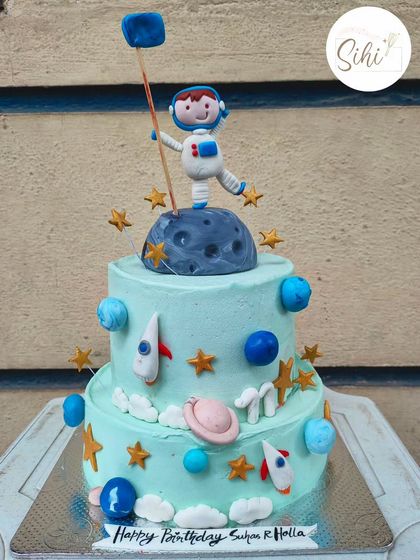 To the moon and stars you aim. This two-tier space-themed cake features a fondant astronaut on the moon, surrounded by rockets, planets, and stars for a budding space explorer.