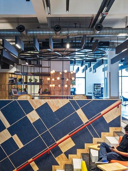 The interior of the Visage office features a vibrant, multi-level design with a central staircase that doubles as seating. The use of colorful upholstery and raw materials creates an energetic and creative atmosphere.