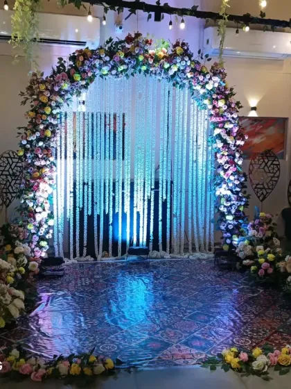 A beautiful floral arch decorated with hanging strings of white flowers. The blue uplighting creates a magical effect, making it a stunning centerpiece or entryway for an evening gala or ceremony.