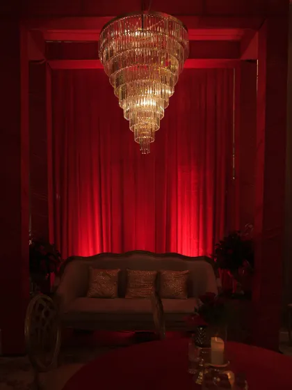 An intimate seating nook created with a classic sofa set against rich red drapes and under a stunning tiered chandelier. It provided a cozy space for guests to relax and chat amidst the grand celebration.