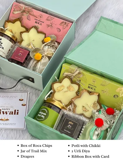 Our twin box hampers are a client favorite. This set features two color-coordinated boxes, one in mint green and one in pink, filled with roca chips, trail mix, urli diyas, and more.