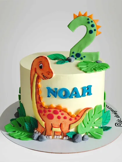 A simple and cute dinosaur cake for a second birthday. This design features a hand-painted dinosaur on a smooth whipped cream finish, surrounded by edible leaves.