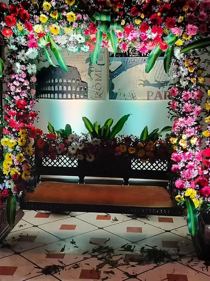 A floral swing setup perfect for taking pictures during a home event. The swing is framed by a dense arch of multi-colored flowers, creating a beautiful and festive photo opportunity for guests.