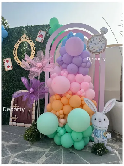 A whimsical photo spot with a rainbow-colored balloon arrangement, a plush white rabbit, and a small door prop.