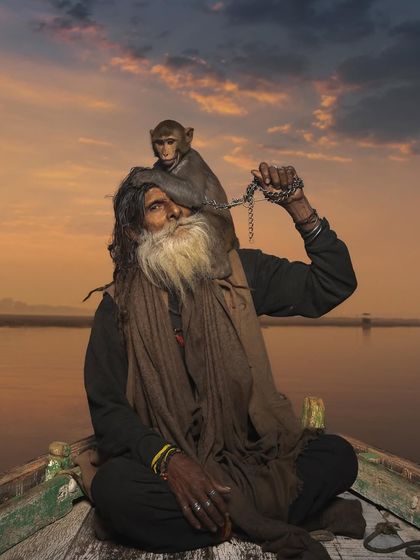 Monkey Baba and his companion on a boat during a beautiful sunset over the Ganga. The warm light adds a sense of peace and finality to their timeless story.