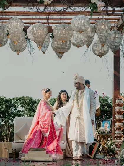 A rustic mandap with a wooden frame, adorned with hanging crystal chandeliers and pastel floral arrangements.