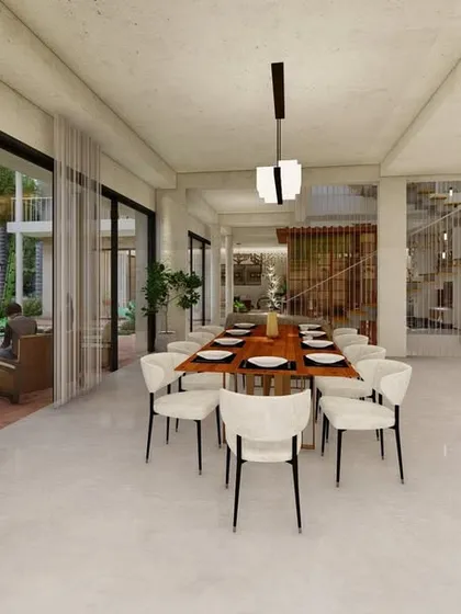 An expansive dining area in an open-concept layout, featuring a long wooden table that can seat a large group. The space is surrounded by floor-to-ceiling glass doors that open to the garden.