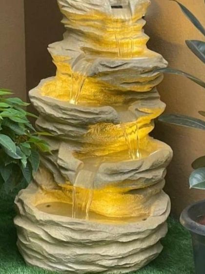 This rock cascade water fountain with built-in lighting creates a dramatic effect. The warm light illuminates the flowing water, making it a beautiful feature both day and night, perfect for adding ambiance to a garden or patio.