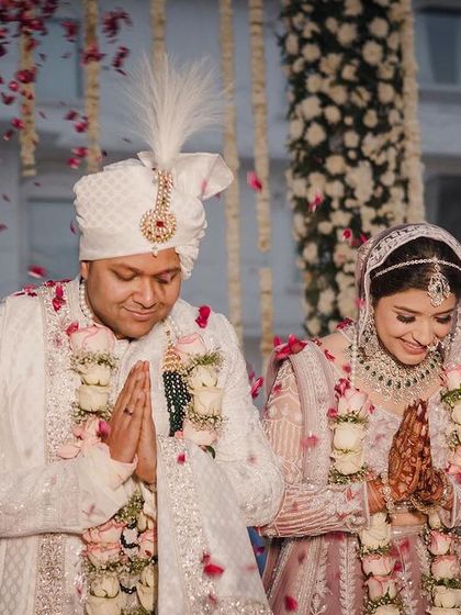 A beautiful moment of gratitude during the wedding ceremony, with the couple showered in rose petals under their elegant floral mandap.