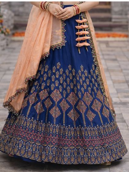 A detailed shot of the lehenga skirt, highlighting the rich blue silk and the traditional woven motifs in gold and pink.