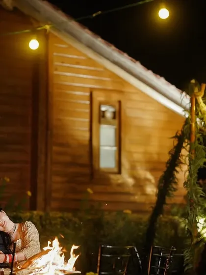 A couple shares a tender moment by a bonfire, the warm glow of the fire and string lights creating a cozy and romantic ambiance.