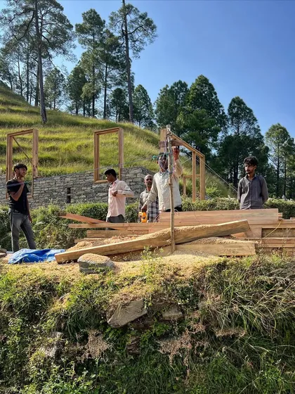 The process of building in the mountains is a partnership with the land and its people. Here, timber frames are being set by local artisans against the backdrop of the Himalayan foothills, a testament to handmade architecture.