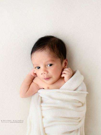 A minimalist portrait of a two-week-old baby wrapped in a simple white cloth. The clean background and direct gaze create a modern and timeless image.