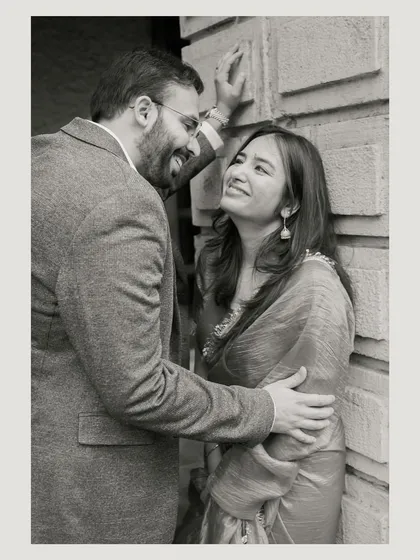 A close, intimate moment shared against a textured wall. The black and white edit emphasizes their expressions and the genuine affection between them.
