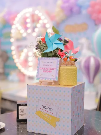Another angle of the charming carnival centerpiece, complete with pinwheels, lollipops, and flowers. The background shows hot air balloon props, highlighting the depth and detail of the event styling.