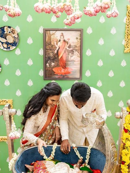 The parents looking lovingly at their daughter in the cradle. The decor includes hanging lotus buds and traditional artwork to create a blessed atmosphere.