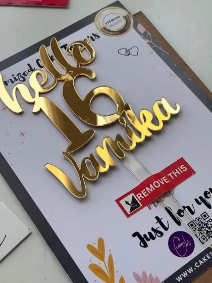 A close-up of the "Hello 16 Vamika" topper, highlighting the "Remove This" sticker on the protective film that keeps it scratch-free during transit.