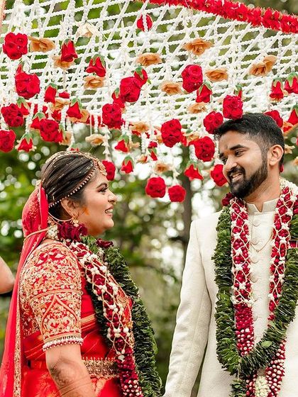 The grand entrance of the bride and groom, surrounded by family. The traditional flower canopy and their shared glance make this a beautiful ceremonial photograph.