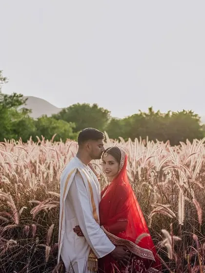 A romantic portrait of a couple in a field of pampas grass, with the hills of Rajasthan in the background. The soft, golden light creates a dreamy and ethereal mood.