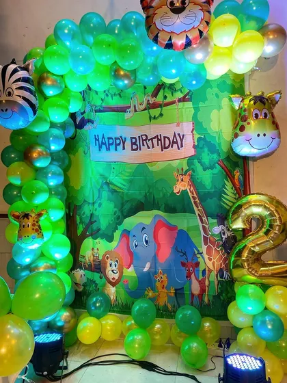 A fun Jungle theme decoration for a second birthday, with a vibrant backdrop, green balloon arch, and animal-shaped foil balloons.