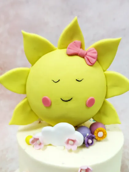 A close-up of the adorable sleeping sunshine topper, complete with a little pink bow and rosy cheeks.