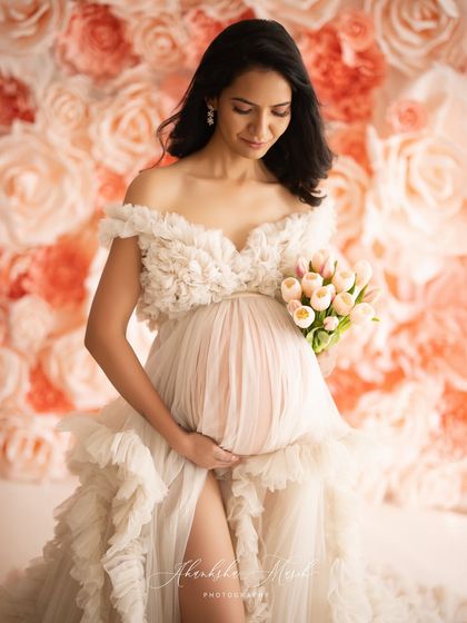 A gentle moment of connection, as the mother-to-be looks down at her bump, surrounded by a wall of soft pink and cream roses.