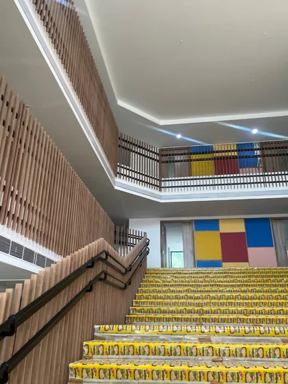 A work-in-progress shot of a staircase in a new school. The image shows the interplay of color and texture with yellow tiled steps and wooden slat railings, setting the stage for a vibrant interior.