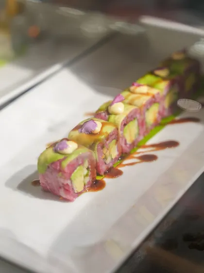 A colourful sushi roll featuring pink-hued rice and fresh avocado, drizzled with a savory sauce. My sushi is as visually appealing as it is delicious.