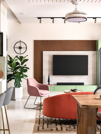 This living room is all about a playful yet sophisticated use of color. A pastel green TV unit is flanked by a pink armchair and a vibrant orange sofa, all tied together with a graphic rug and warm wood paneling.