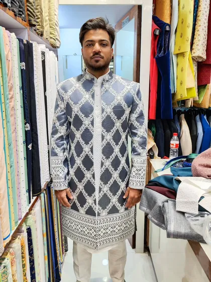 A modern open sherwani in a sophisticated grey, featuring a beautiful white geometric embroidery pattern. This outfit is layered over a sequined kurta and pant for a touch of sparkle.