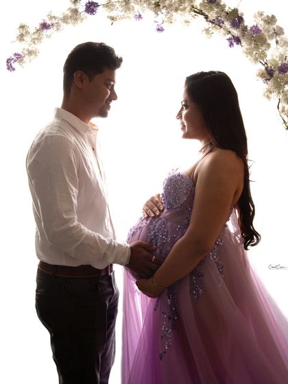 A dreamy, high-key silhouette of a couple sharing a look under a floral arch. A romantic and artistic maternity portrait.