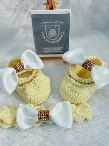 An elegant accessory set in a soft yellow, this includes booties and a headband decorated with large white satin bows that have a sparkly center.