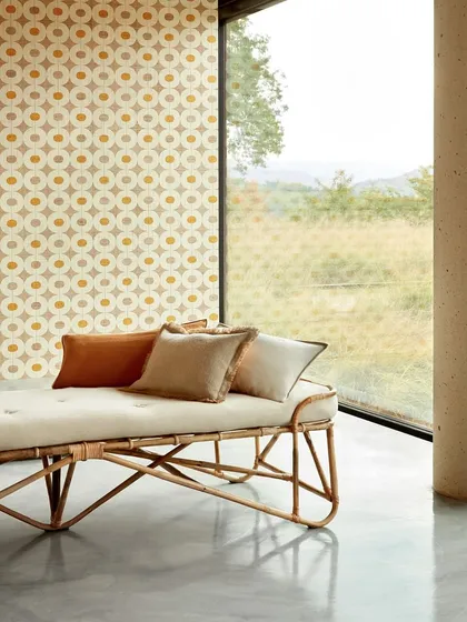 A minimalist daybed with a natural rattan frame and comfortable upholstered mattress. Set against a wall of geometric raffia wallpaper, this scene illustrates our ability to blend natural materials with modern design for a look that is both organic and sophisticated.