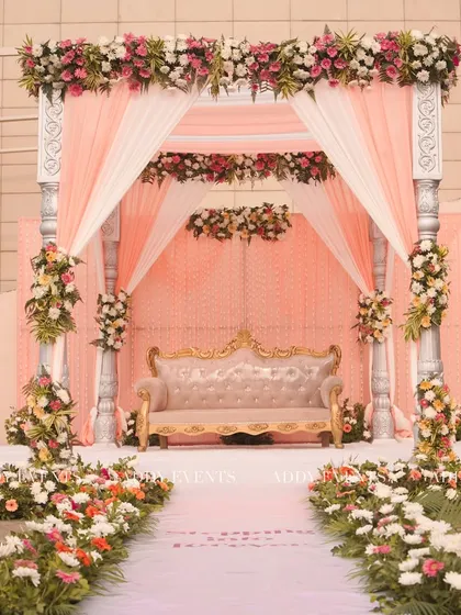 This elegant mandap features soft peach draping, classic silver pillars, and lush floral arrangements. The design creates an intimate and romantic setting, perfect for a day wedding ceremony.