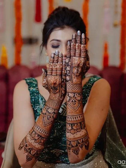 A stunning bride with her hands full of dreams and intricate henna. The peek-a-boo pose is a classic for showing off bridal mehendi.