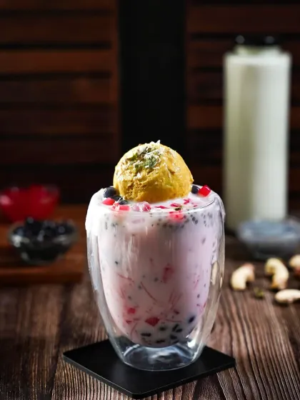A glass of falooda-inspired boba tea topped with a scoop of mango ice cream. The moody lighting and dark wood background make the colors of the drink and its many textures stand out.