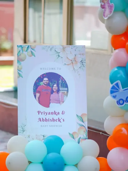 A personalized welcome sign for Priyanka and Abhishek's baby shower. The sign features a photo of the happy couple, adding a lovely personal touch to the event entrance.