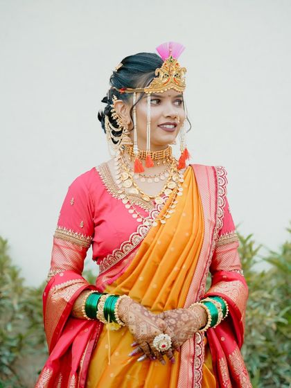 A beautiful bride in a traditional yellow and pink Nauvari saree. Her look is completed with a classic Maharashtrian bridal crown, a choker, and a floral bun, ready for her wedding rituals.