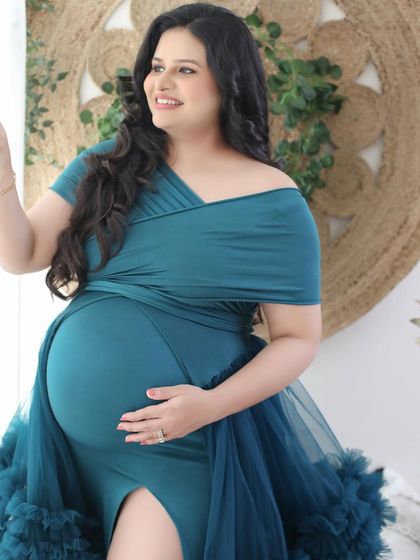 A joyful and confident pose by the window. This mom-to-be radiates happiness in a teal convertible gown, set against a bright, boho-inspired backdrop.