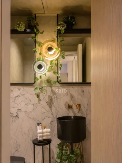 This powder room uses a black pedestal basin and dramatic lighting against a white marble backdrop. The addition of climbing ivy brings a touch of nature and softness to the bold, high-contrast design.