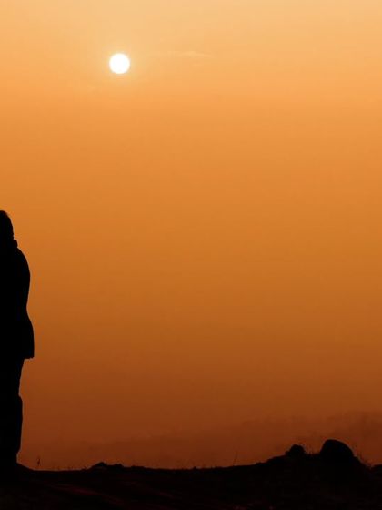 An intimate silhouette of a couple against a warm, orange-hued sunset. This romantic pre-wedding photo focuses entirely on their connection, framed by the evening sky.