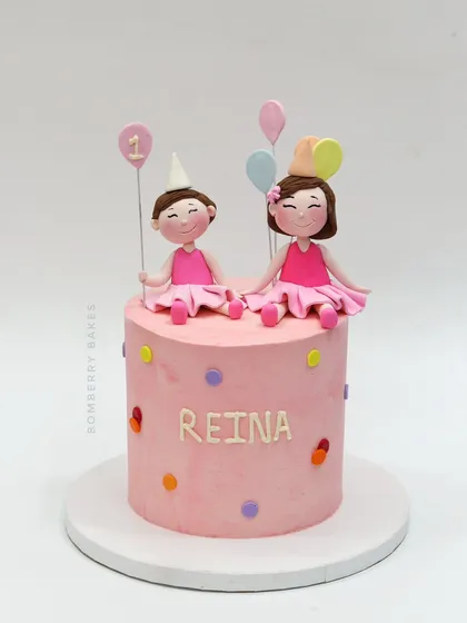 A simple and sweet pink cake for a first birthday, topped with two adorable girl figurines.