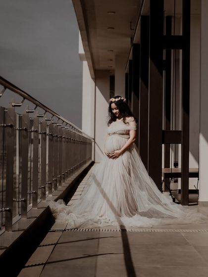 A dramatic and artistic maternity portrait of a woman in a flowing gown, standing on a balcony. The play of light and shadow adds a beautiful, moody quality to this pregnancy photoshoot.