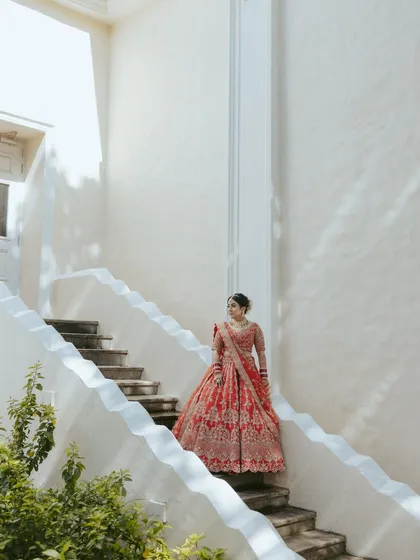The bride descending a pristine white staircase, her red lehenga providing a stunning pop of color. This shot is all about grace, elegance, and architecture.