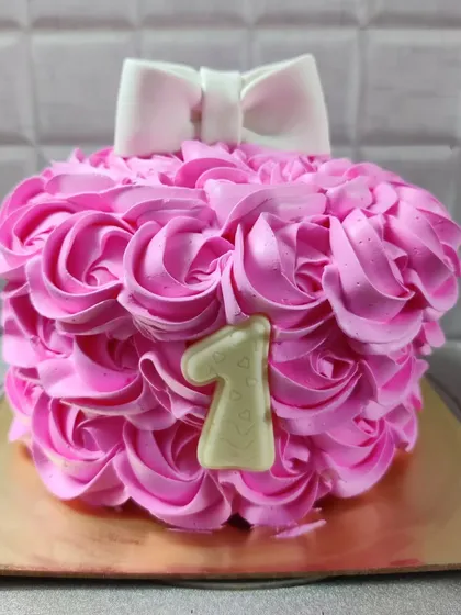 A pretty pink rosette cake for a first birthday. The design is simple, elegant, and topped with a white fondant bow.