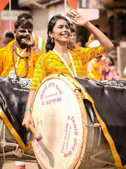 A candid black and white shot of a female dhol player, her smile lighting up the frame.