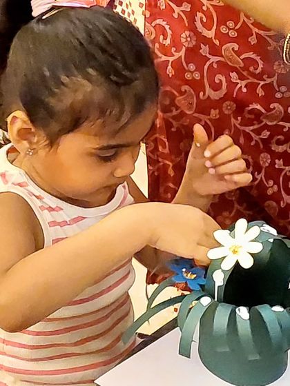 A toddler carefully assembles her flower basket for Mother's Day. Even the littlest hands can create something beautiful.