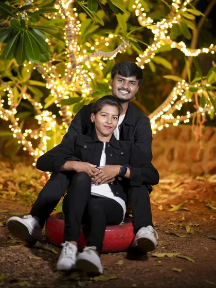 A happy and playful moment with the couple sitting on a decorated tire swing under a tree wrapped in lights.