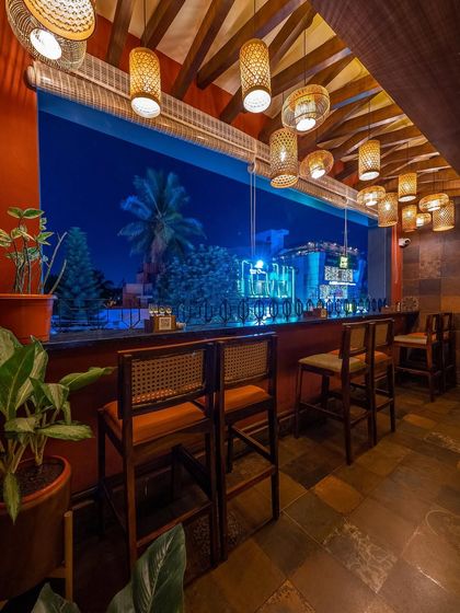 This high-seater bar area offers a fantastic view through a large picture window. The warm tones of the wood, leather, and hanging cane lights create a cozy and inviting spot to enjoy the evening.