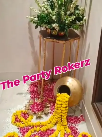 A creative entrance decor element for Teej, featuring a brass pot (kalash) from which marigold garlands and flower petals are spilling out.